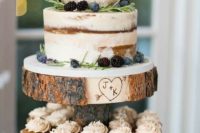 a naked fall wedding cake with blackberries and blueberries, with greenery and some blooms served on a wood slice stand