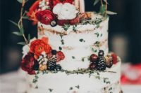 a naked wedding cake decorated with bold blooms, greenery, gilded berries and twigs for a summer wedding