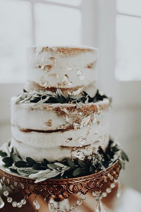 a naked wedding cake with greenery and gold leaf is a chic idea for a neutral wedding with a rustic feel
