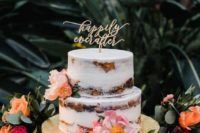 a naked wedding cake with pink and peachy blooms and a calligraphy topper for a summer or tropical wedding