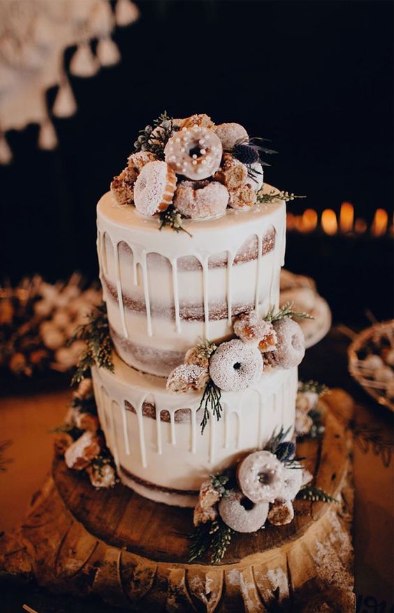 a naked wedding cake with white chocolate drip, greenery, glazed donuts and thistles for a winter wedding