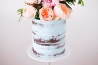 a pale blue naked wedding cake with n oversized fresh floral topper looks wow