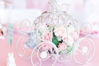 a refined white carriage filled with fresh blooms and greenery is a cute and chic Disney themed wedding centerpiece