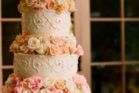 a romantic wedding cake with patterned tiers and peachy and pink blooms between the tiers