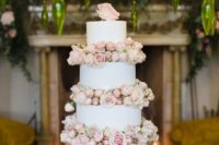 a romantic white wedding cake with blush blooms and a blush rose on top is very beautiful