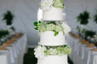 a rustic white wedding cake with textural tiers, green and white blooms between the tiers