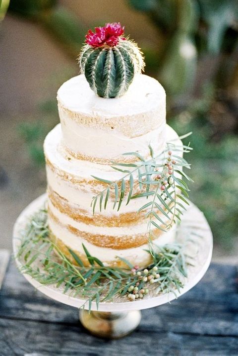 a semi naked wedding cake topped with a cactus and decorated with greenery for a desert wedding
