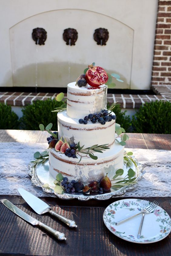 a semi naked wedding cake topped with fresh greenery and fruits on top for a cool fall wedding