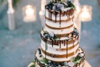 a statement naked wedding cake with sugared berries, greenery, silver chocolate coins and chocolate drip