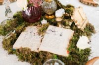a story book wedding centerpiece composed of moss, a story book, candles, a crown on a stand and a floral arrangement