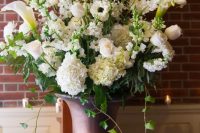 a super lush wedding arrangement of white roses, anemones, calla lilies and lots of greenery in vintage urns is amazing
