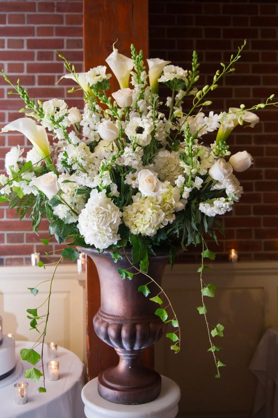 a super lush wedding arrangement of white roses, anemones, calla lilies and lots of greenery in vintage urns is amazing