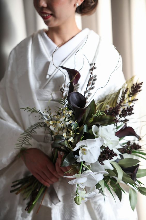 a textural wedding bouquet of greenery, white orchids and dark purple callas, grasses and twigs is a unique and beautiful idea