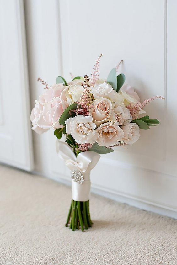 a very delicate and chic blush wedding bouquet of roses, astilbe and some greenery with a white ribbon wrap and a glam brooch is cool
