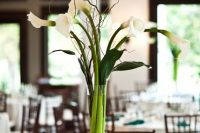 a wedding centerpiece of a clear vase with calla lilies, twigs and leaves is amazing for spring or summer