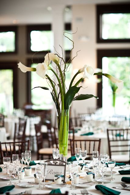 a wedding centerpiece of a clear vase with calla lilies, twigs and leaves is amazing for spring or summer