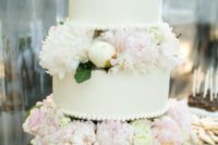 a white wedding cake with white and blush blooms and leaves between the tiers is wow