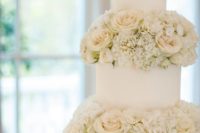 a white wedding cake with white blooms between the tiers is very chic and very elegant