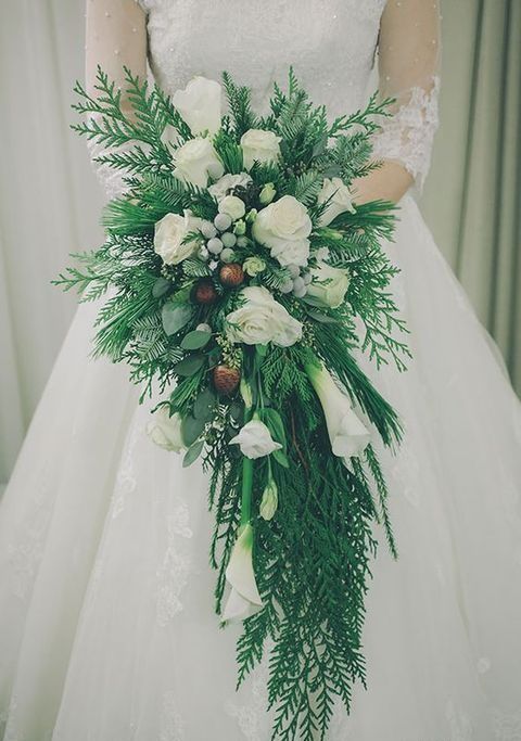 a winter wedding bouquet of lots of greenery and fern, white roses and calla lilies, berries and pinecones is super chic