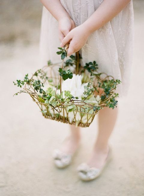 a woven see-through basket decorated with greenery and with petals inside
