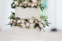an elegant white wedding cake with blush flowers and greenery between the tiers