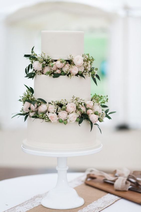an elegant white wedding cake with blush flowers and greenery between the tiers