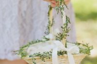 an ivory basket with greenery and a white ribbon bow plus petals inside is a beautiful and refined idea