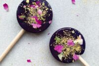 dark lollipops with gold glitter and some flwoer petals are a nice idea for a moody fall wedding, you can DIY them