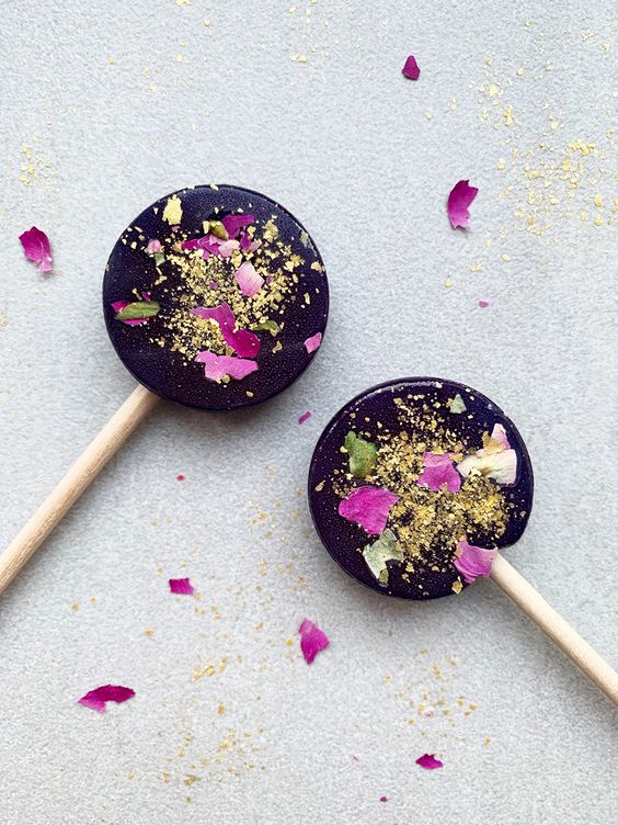 dark lollipops with gold glitter and some flwoer petals are a nice idea for a moody fall wedding, you can DIY them
