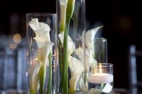 tall glasses with calla lilies and floating candles plus more candles around compose a chic wedding centerpiece