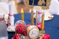 the Beauty and the Beast wedding centerpiece with a clock, red roses and fake candles plus a framed table number