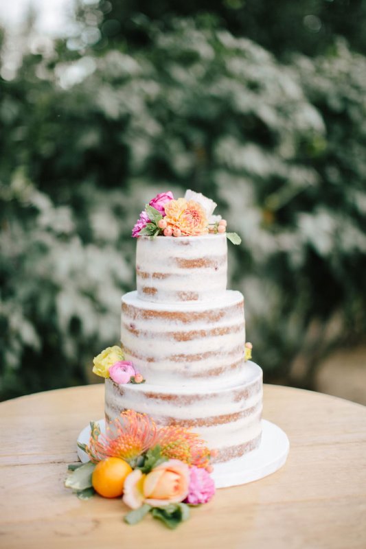 a naked wedding cake with bright blooms on top and citrus is a nice idea for a summer or tropical wedding