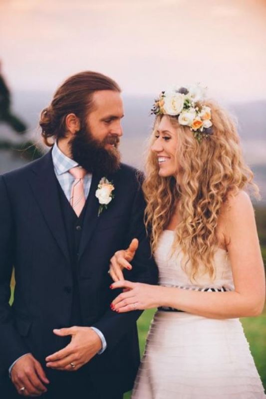 a summer boho groom's look with a three-piece grey pantsuit, a pink tie, a full beard and a man bun is bold and chic