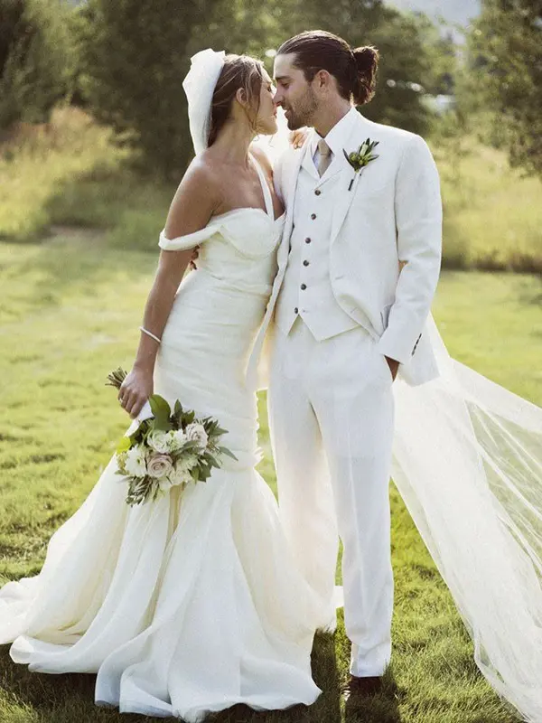 a white three-piece wedding suit, a white shirt, brown shoes, a green boutonniere and a trendy man bun to give a fashion-forward look to it