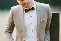 an elegant barn groom look with a camel blazer, a white shirt with black buttons, grey pants, a burgundy bow tie and a brown belt
