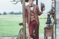 a vintage barn groom’s look with burgundy pants, a rust blazer and waistcoat, a black bow tie, a rust hat and purple shoes