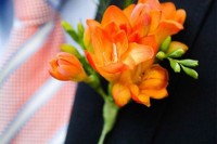 a bold orange freesia wedding boutonniere with greenery is a lovely color accent to the groom’s or grooman’s look
