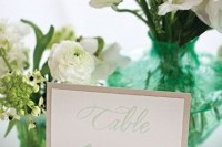 a white cluster wedding centerpiece of vases with white freesias and other blooms and greenery and a table number is a cool and easy to repeat idea