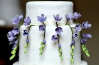 a white wedding cake decorated with purple sugar freesias and greenery is a lovely idea with a touch of color