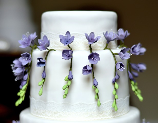 a white wedding cake decorated with purple sugar freesias and greenery is a lovely idea with a touch of color