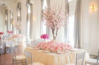 a refined neutral wedding reception space with a neutral table with pink blooms on the table and faux cherry blooming trees as an addition for a wow factor