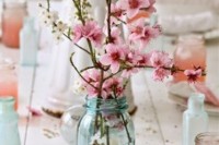 a delicate wedding centerpiece of a blue jar with pink cherry blossom is a lovely idea for a laid-back wedding, a backyard or some other non-formal one