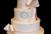 a neutral wedding cake with shiny ribbons and brooches, monograms and patterns plus fresh blooms on top