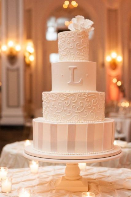 a white wedding cake with patterned and a striped tier, plus a monogram and a sugar bloom on top is a stylish and tasty idea