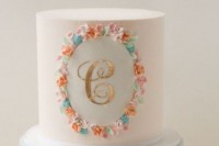 a white wedding cake with colorful blooms and a gold monogram is a stylish idea for those who love colors