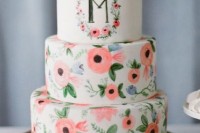 a white wedding cake with painted blooms and a monogram is a stylish and fun idea for a spring or summer wedding