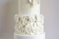 a refined white wedding cake with sleek, floral and beaded tiers, sugar blooms and a gold feather on top