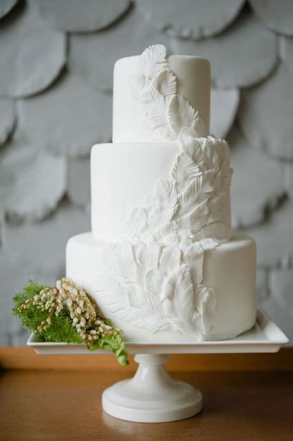a romantic plain white wedding cake with feathers going up the cake is a very chic and elegant idea