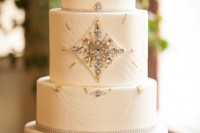 a white art deco wedding cake with patterns and embellishments, beads and feathers on top for a 20s wedding
