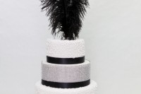 a black and white wedding cake with patterned and embellished tiers, black ribbons and black feathers on top